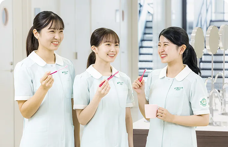 画像：制服を着た女性3人が笑顔で歯ブラシを持っている様子。